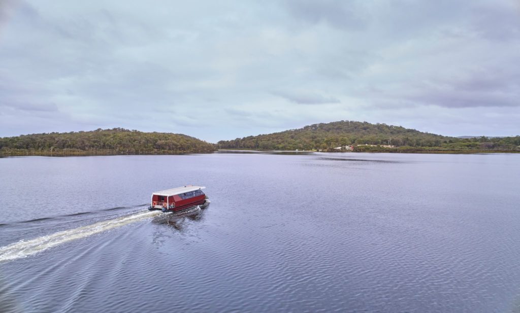 A landscape image of a small ferry putting across an inlet with trees in the distance shows nature and experiences had on The South West Edge road trip