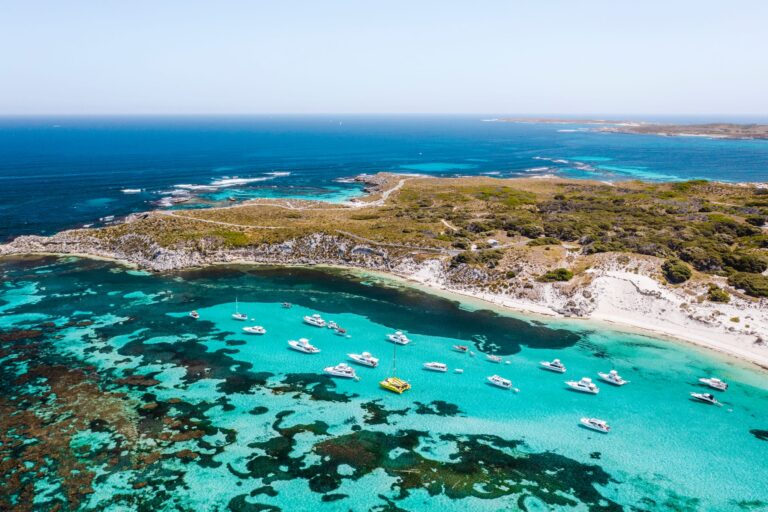 A pristine turquoise bay on Rottnest Island, with boats and yachts anchored just offshore.