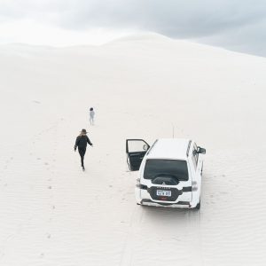 A drone image shows a four wheel drive vehicle and two people on pristine white sand dunes to show adventure in natural landscapes along The South West Edge road trip from perth to esperance